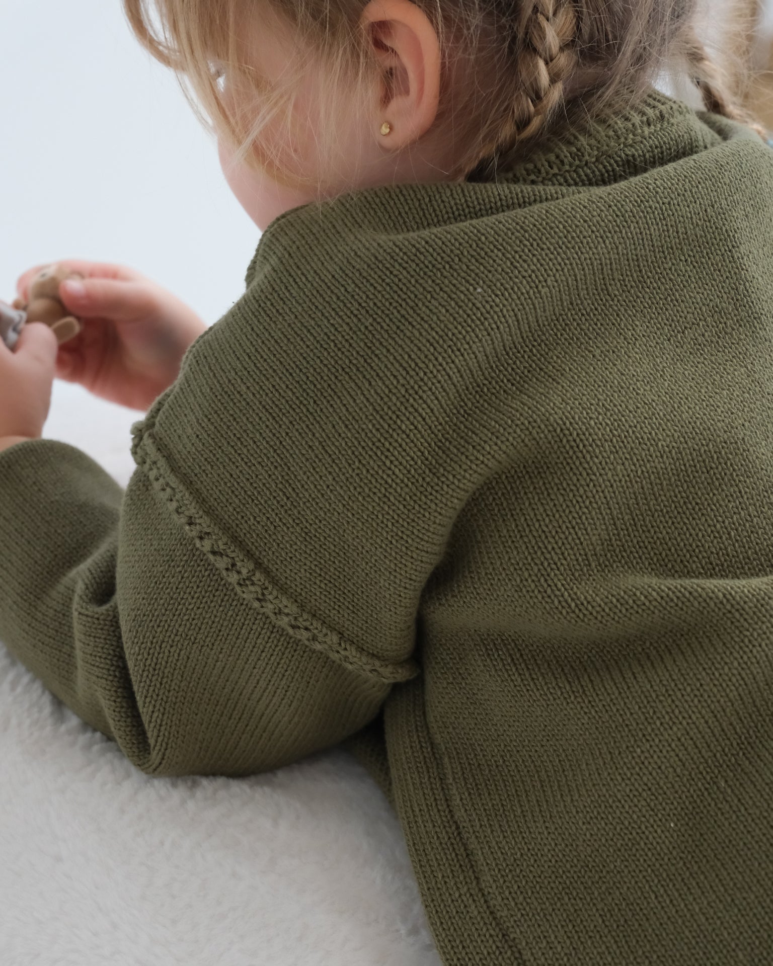 Child wearing a green sweater with braided detailing on a white background