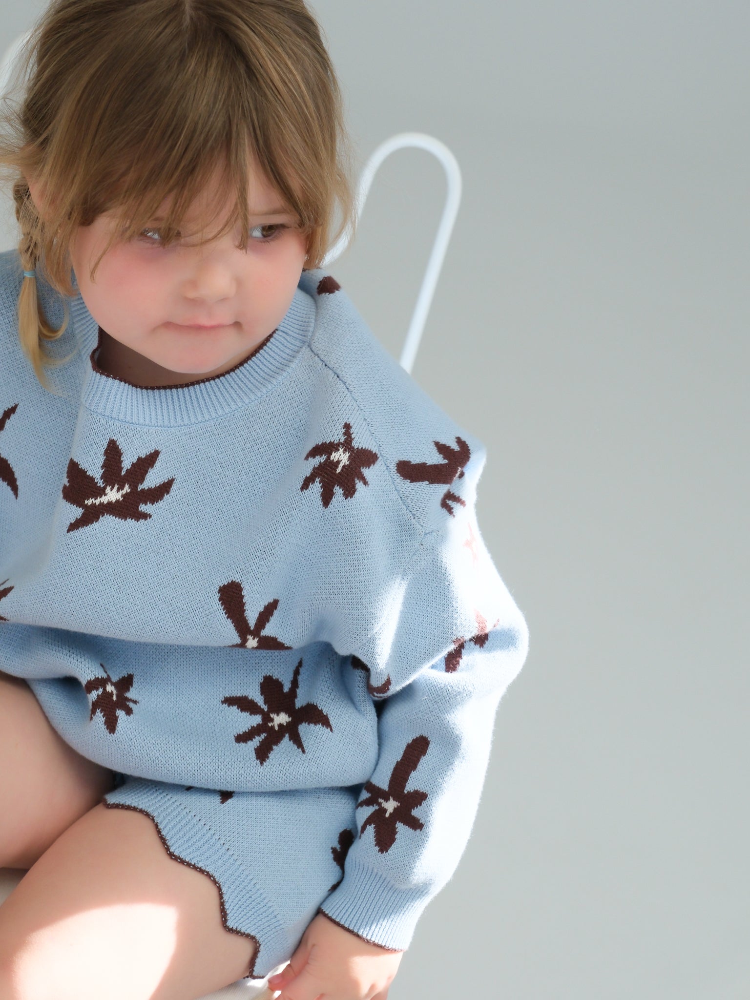Child wearing a blue sweater with brown leaf patterns on a plain background