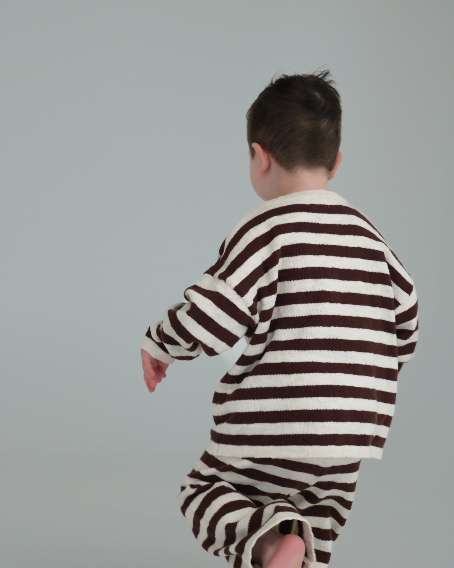 Child wearing a brown and white striped outfit on a plain background