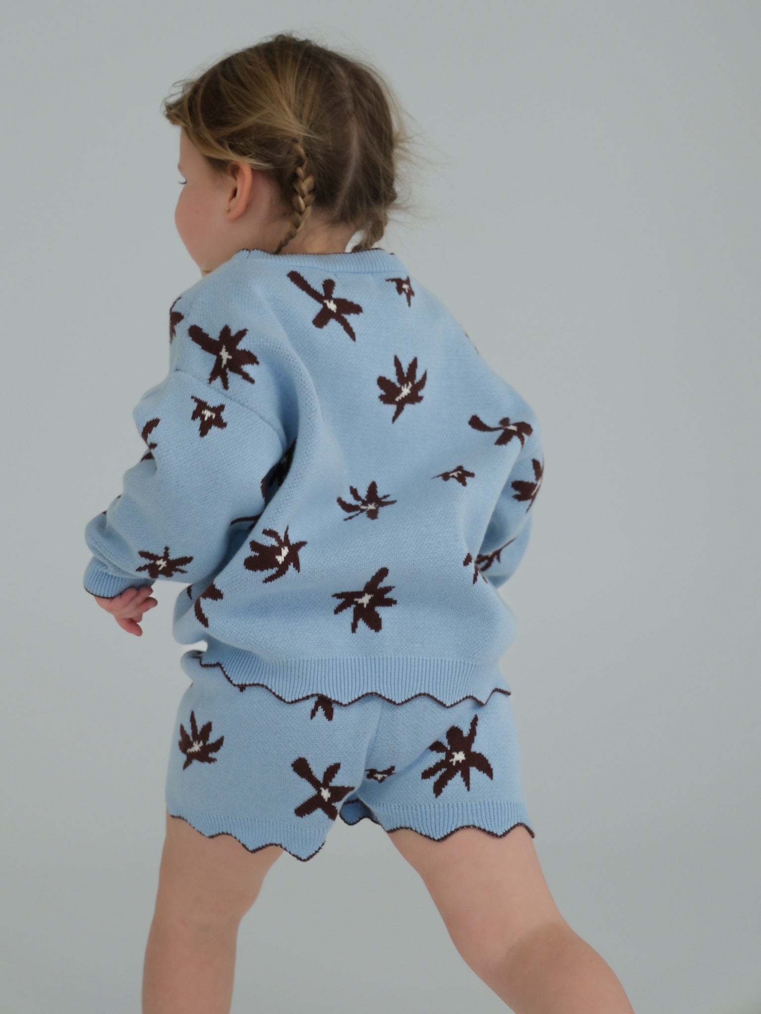 Child wearing a blue outfit with brown patterns on a plain background