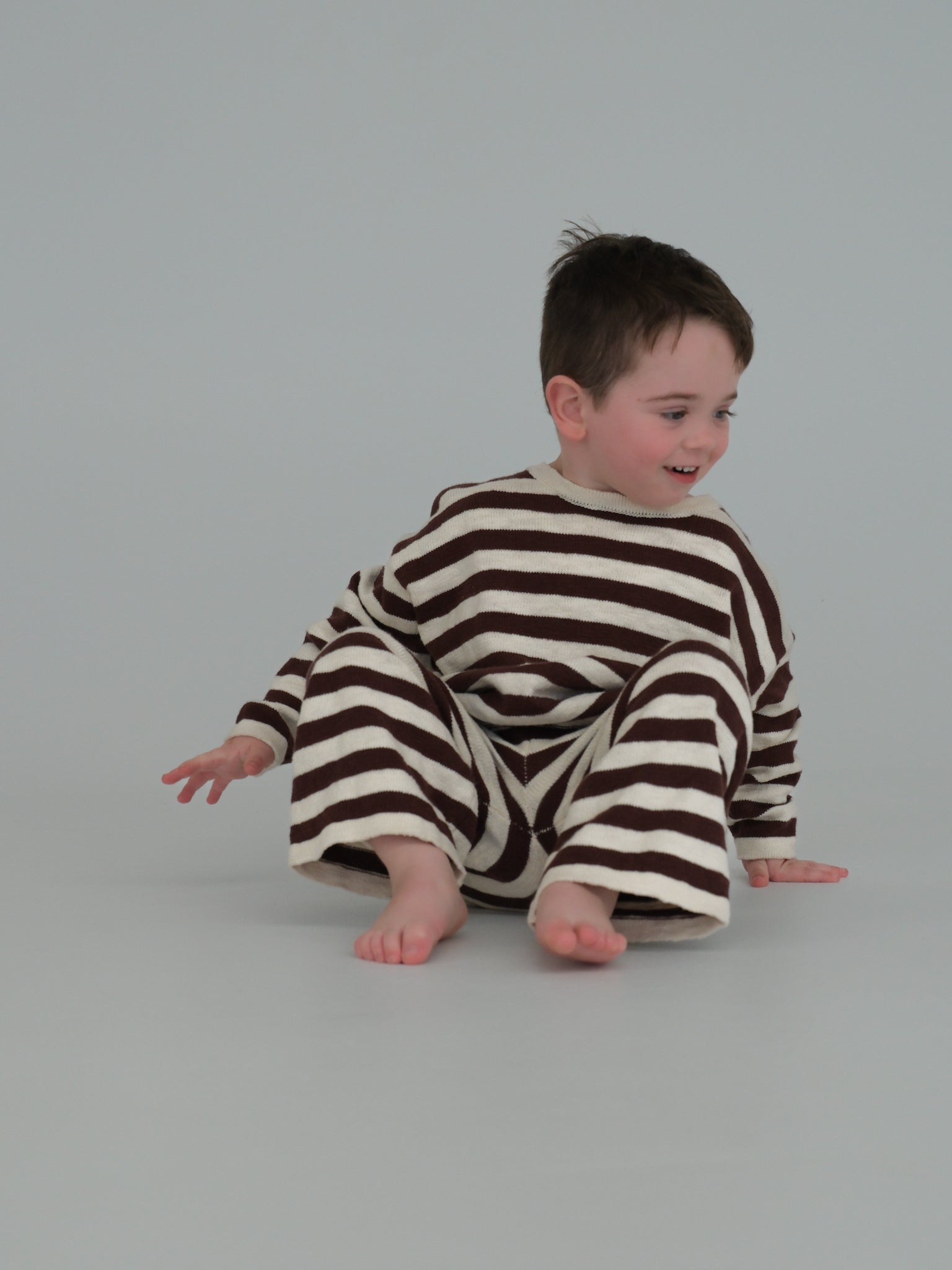 Child wearing a brown and white striped outfit on a plain background