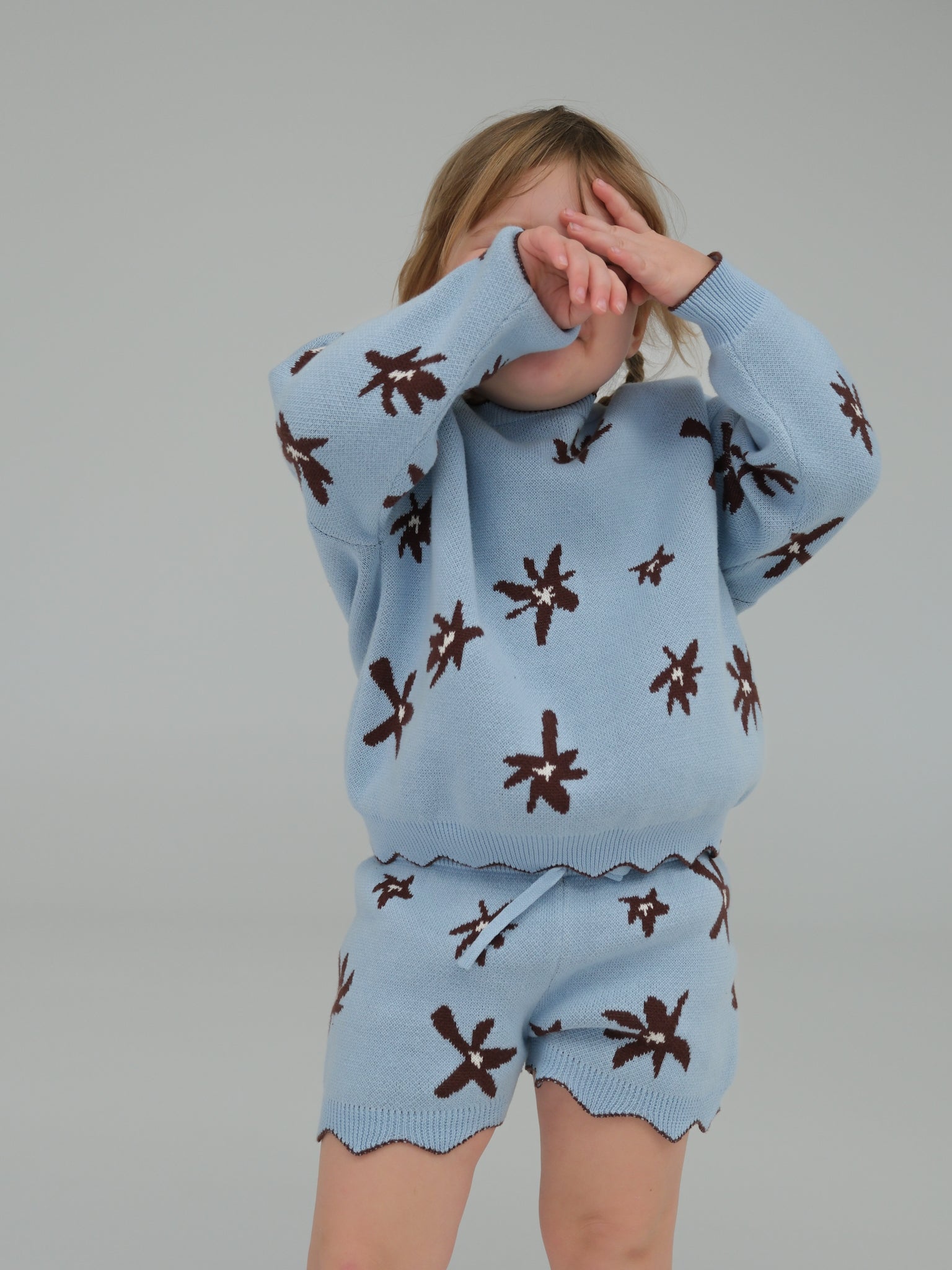 Person wearing a light blue sweater and shorts set with brown patterns on a plain background