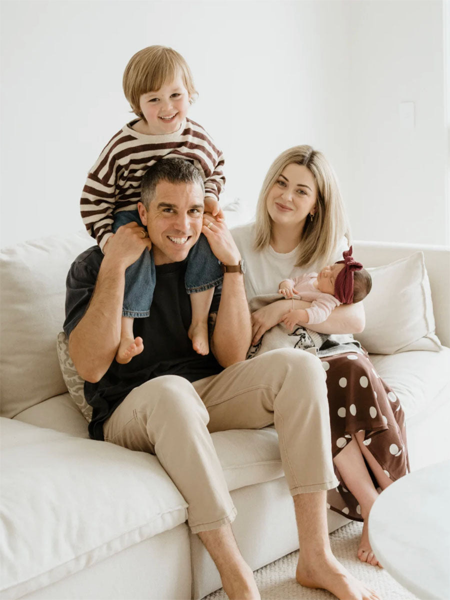 Family of four sitting on a couch in a bright living room.
